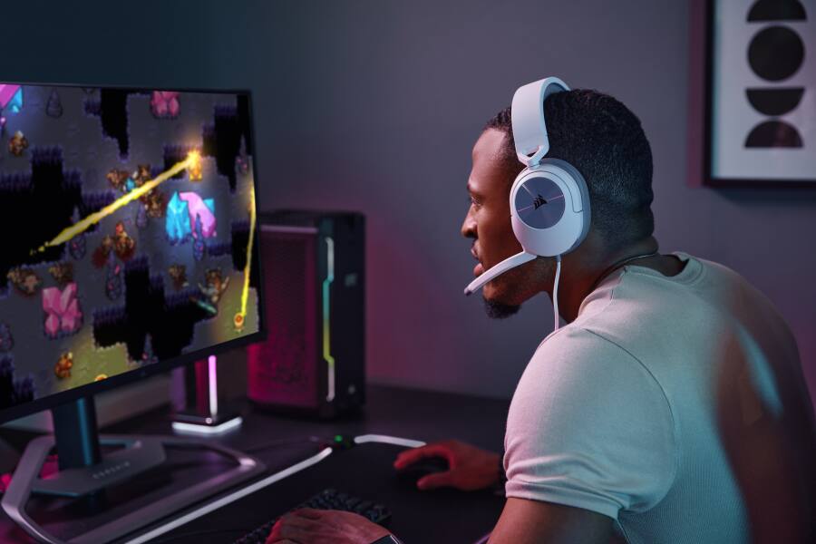 Persona frente a su PC jugando a videojuegos con auriculares para juegos HS55 SURROUND blancos. 